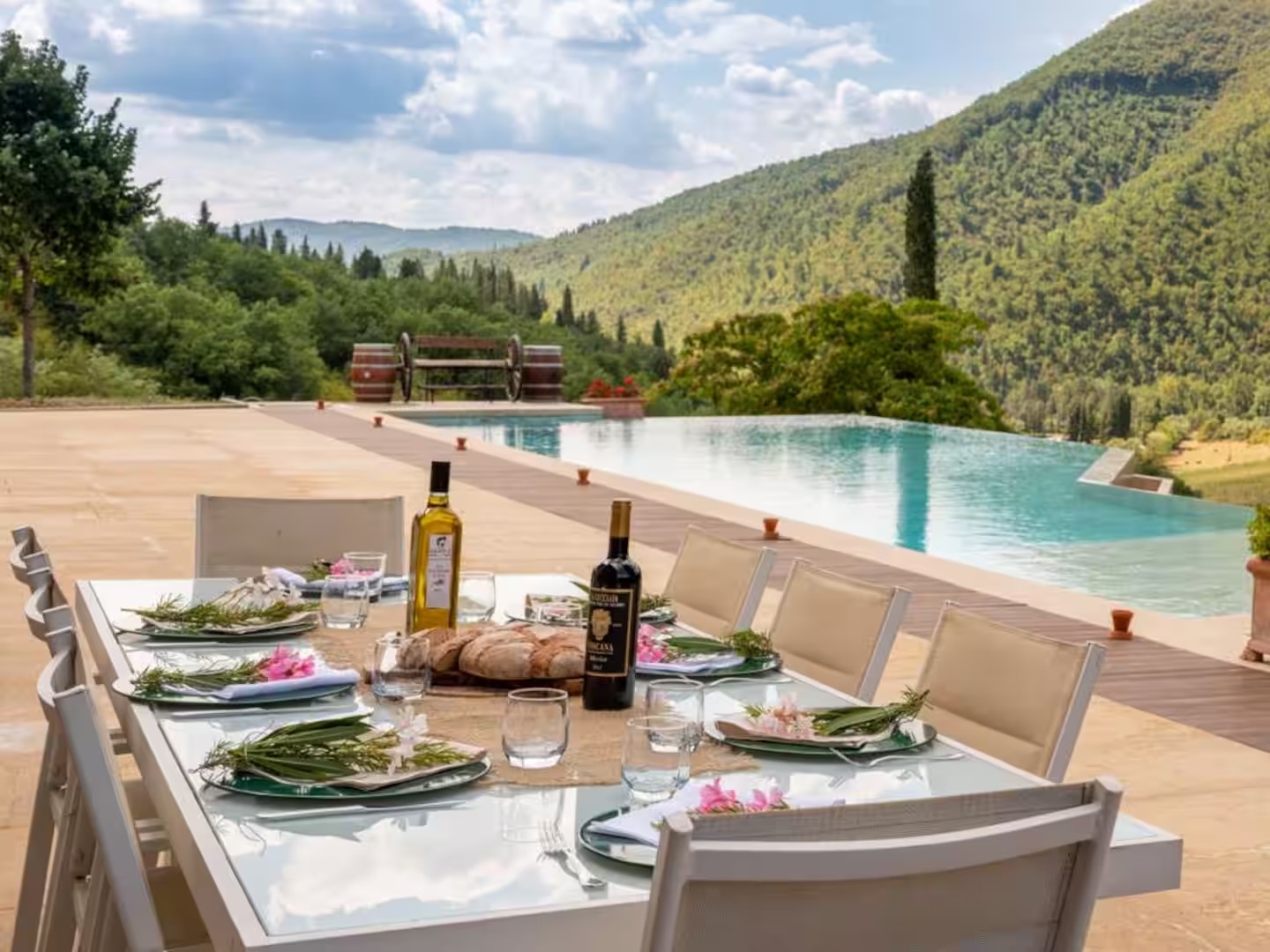 An outdoor table beside the villa pool with Tuscan hills beyond