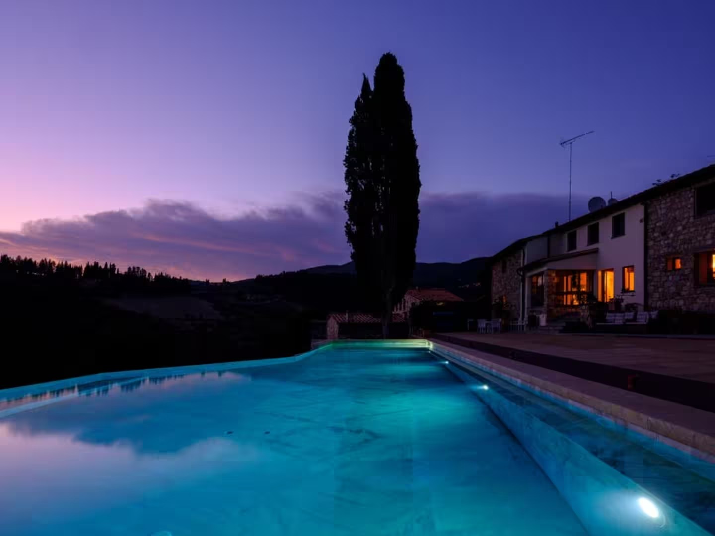 The illuminated villa pool and cypress tree at dusk