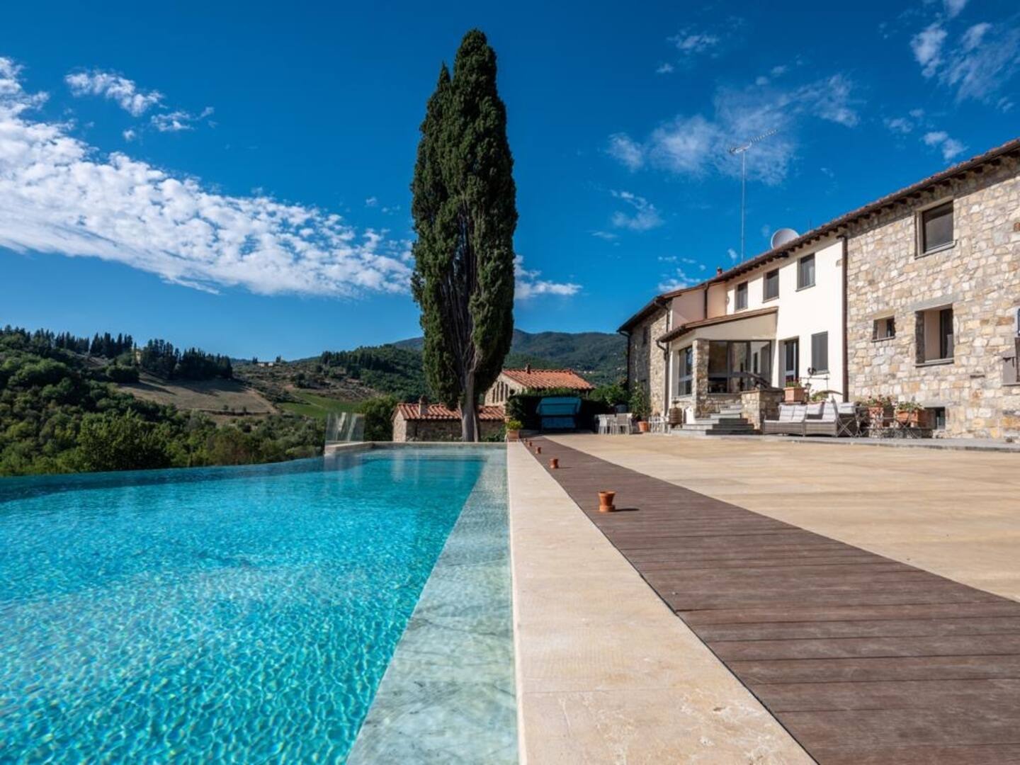 Stone Tuscan villa beside a turquoise pool and cypress tree